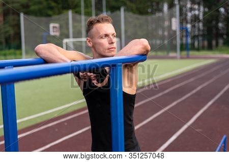 A Muscular Man Stands Leaning On Parallel Bars, With A Bare Torso.