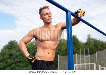 A Muscular Man Stands Near Parallel Bars, With A Bare Torso.