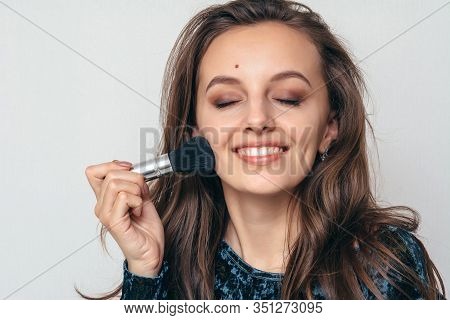 Beautiful Young Woman In Shiny Green Dress Applying Powder With A Brush To The Face.