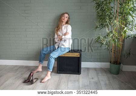 Young Beautiful Woman Sitting On Subwoofer With Bare Feet Next To Green Plant