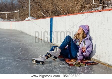 Lovely Young Woman Relaxing After Riding Ice Skates And Drinking Hot Drink From Termo Pot On The Ice
