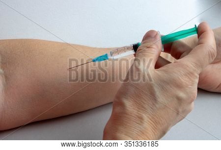 Hand In The Medical Glove With Syringe Prepared To Make An Injection Into Wrinkled Hand On The White