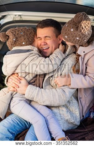 Dad And Daughters In Winter Clothes Sitting In The Trunk Of A Car In The Winter Forest