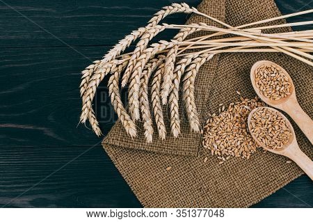 Ears Of Wheat And Spoon Of Wheat Grains On Wooden Table