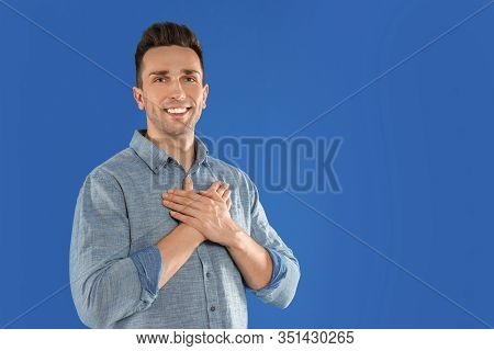 Handsome Grateful Man With Hands On Chest Against Blue Background. Space For Text