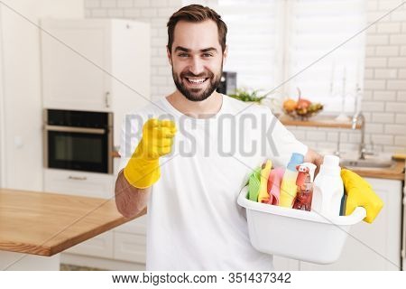 Image of young optimistic positive man househusband indoors pointing to you.