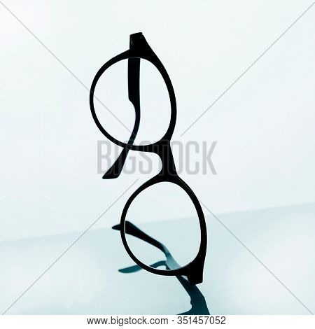 closeup of a pair of black eyeglasses on a reflecting surface against a white background