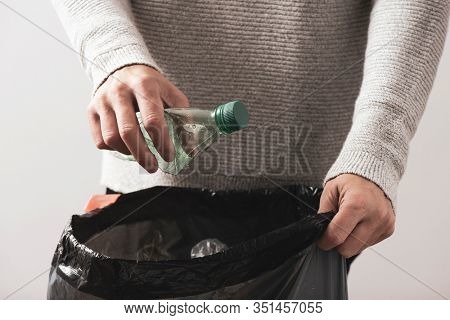 closeup of a young caucasian man about to throw an empty plastic bottle to the trash bin