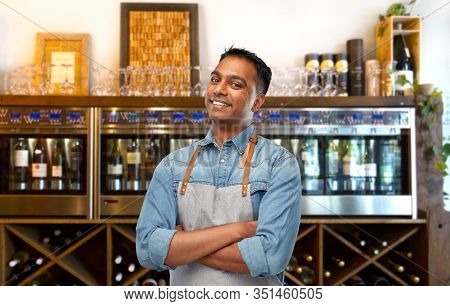 people, job and profession concept - smiling indian barman, waiter or salesman in apron over wine bar background