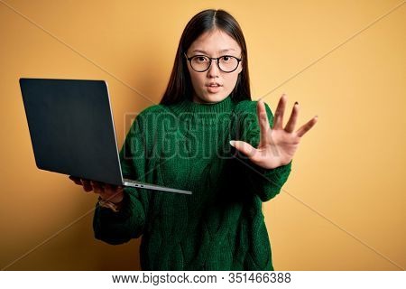 Young asian business woman wearing glasses and working using computer laptop doing stop gesture with hands palms, angry and frustration expression