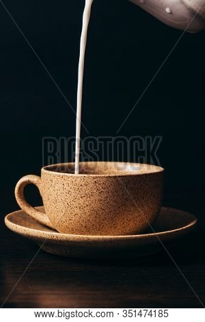 Milk Is Pouring Into A Cup Of Coffee On A Black Background.