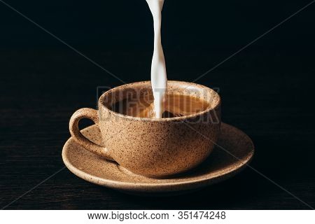 Milk Is Pouring Into A Cup Of Coffee On A Black Background.