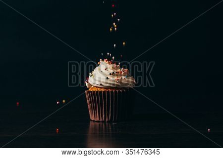 Cupcake Sprinkled With Decorations On A Black Background.