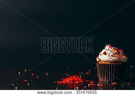 Cupcake Sprinkled With Decorations On A Black Background.