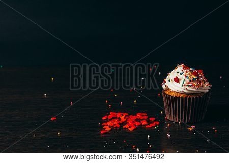 Cupcake Sprinkled With Decorations On A Black Background.