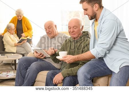 Young Man Taking Care Of Elderly People In Geriatric Hospice