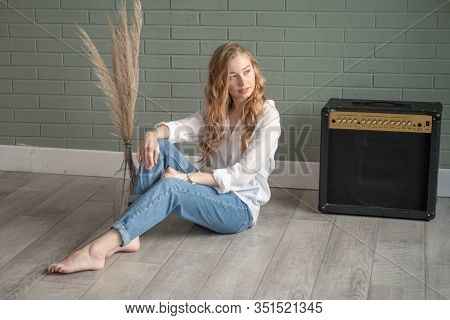 Young Beautiful Woman With Bare Feet Sitting On The Floor Next To Subwoofer And Glass Vase With Dry 