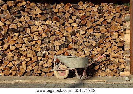 Wheelbarrow In Front Of Fuelwood Stack At Sunny Day