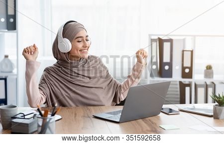 Boost Mood At Work. Joyful Arabic Woman In Hijab Listening Music In Wireless Headphones In Office An