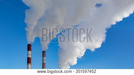 Two Chimneys Pipes With Thick White Smoke Against A Clear Blue Sky. Air Pollution, Environmental Pro
