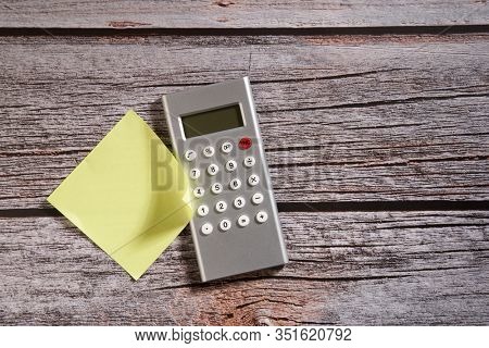 calculator and yellow stickey note on the wooden background