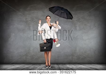 Young Business Woman Multitasking With Different Staff In Hands. Over Gray Wall Background.