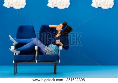 Side View Of African American Sitting On Seats, Listening To Music On Blue Background With Clouds