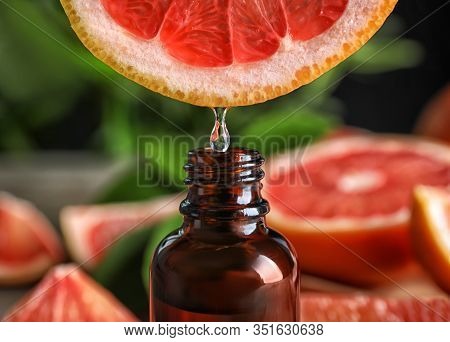 Citrus Essential Oil Dripping From Grapefruit Slice Into Bottle, Closeup