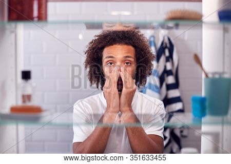 View Through Bathroom Cabinet Of Man Getting Ready For Work And Moisturizing Skin