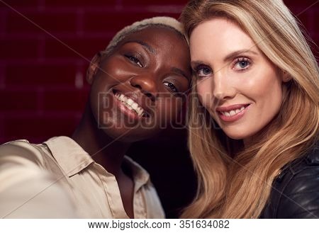 Two Young Female Friends Posing For Selfie Reflected In Mirror Of Bathroom In Club