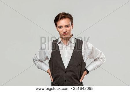 Young Man In A White Shirt And Grey Vest In High Dudgeon Over Grey Background.