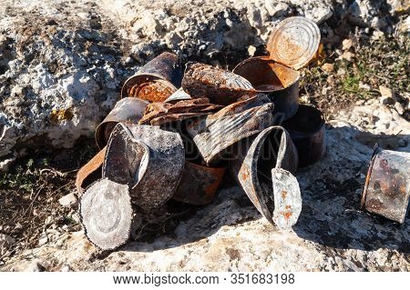 Group Of Old Rusty Tin Cans Covered With Ash On Stones At Sunny Day. Concept Of Environmental Pollut