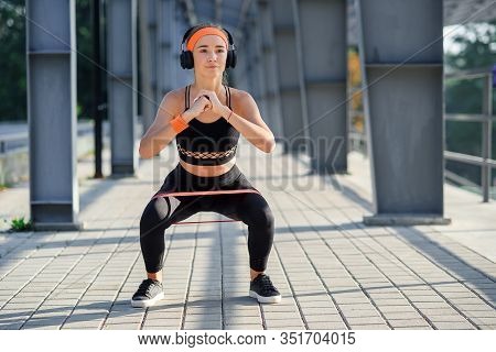 Fitness Girl With Earphones Which Doing Squat Exercises With Fabric Booty Band During Her Sport Work