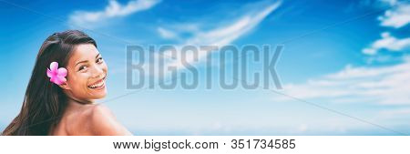 Asian beauty skincare model smiling against blue sky banner panoramic with copyspace on background header. Tropical summer model healthy hair with monoi flower.
