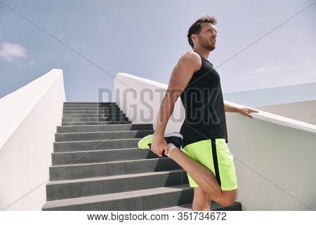 Fitness man runner getting ready to run stretching legs warm up quad stretch exercise on outdoor staircase cardio HIIT workout.