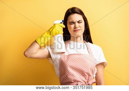Young Housewife In Apron And Rubber Gloves Imitating Self-killing With Spray Bottle With Closed Eyes