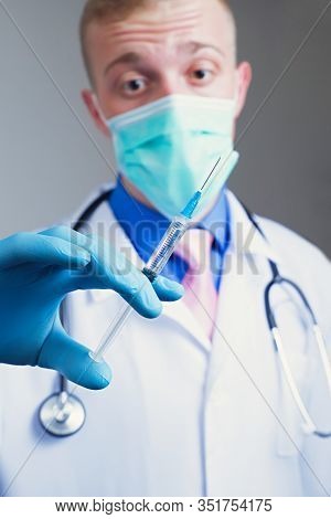 Scared Young Doctor In Gauze Mask And Medical Robe Holding Syringe In His Blue Rubber Glove Dressed 