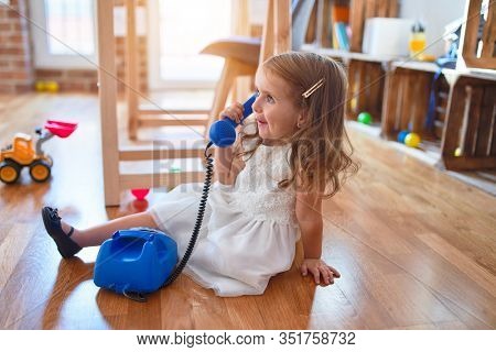 Adorable blonde toddler playing with vintage phone. Sitting on the floor around lots of toys at kindergarten