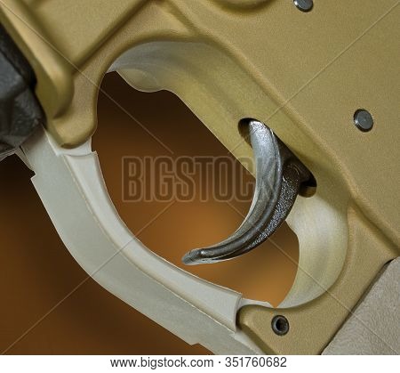 Brass Looking Ar-15 With Black Trigger And Shadow On Brown Background