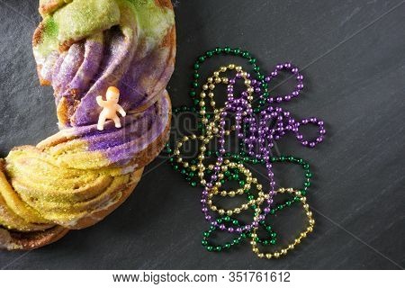A Traditional Plastic Baby Jesus Figurine Rests On A Festive Green, Purple And Gold Mardi Gras King