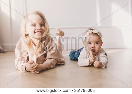 Two Cute Sisters Sitting On Floor And Playing At Home.little Sister Hugging Her Smalest Sister. Todd