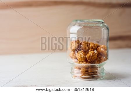 closeup of some nueces de macadamia garrapinadas, spanish candied macadamia nuts, in a glass jar upside down on a wooden table