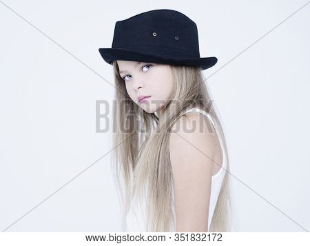 little pretty girl in black classic hat. Studio ashion photography of kid in white dress. Beautiul model on white background.