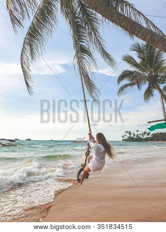Toned Photo Of Beautiful Young Wman Swinging On The Palm Tree At Beach