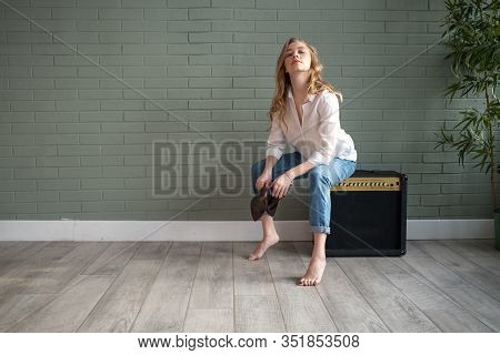 Young Beautiful Woman Sitting On Subwoofer With Bare Feet Next To Green Plant