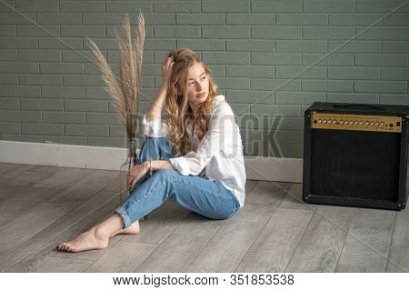 Young Beautiful Woman With Bare Feet Sitting On The Floor Next To Subwoofer And Glass Vase With Dry 