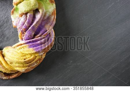 Partial View Of A Festive Green, Gold And Purple Mardi Gras King Cake On A Gray Slate Background Wit