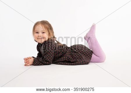 Attractive Little Child In Dress Liying On The Floor And Looking At The Camera Isolated Over White B