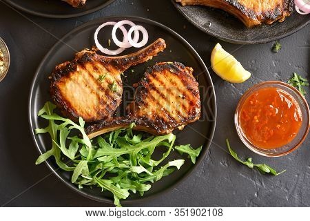 Grilled Pork Steaks On Vlack Plate Over Dark Stone Background. Top View, Flat Lay