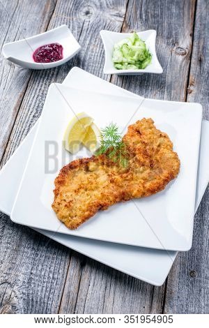 Traditional deep fried Wiener schnitzel from veal topside with cucumber salad and cranberry jam offered as closeup modern design plate on a rustic wooden board 